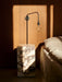 A bedroom scene featuring the black Staple Lamp and a tall marble Plinth as a bedside table, with dramatic natural light.