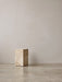 The Plinth Tall in Kunis Breccia marble stands on a polished terrazzo floor in a minimalist room against a neutral wall.
