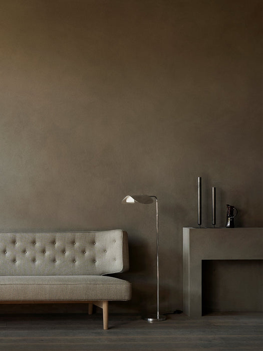 In a dim room, the grey Radiohus Sofa with tufted backrest is shown next to a silver Wing Floor Lamp and a Plinth Pedestal.
