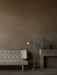 In a dim room, the grey Radiohus Sofa with tufted backrest is shown next to a silver Wing Floor Lamp and a Plinth Pedestal.