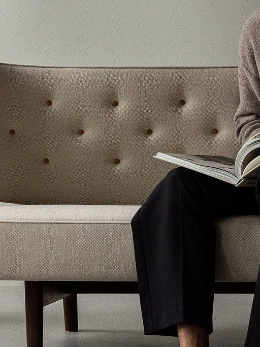 A person reads a magazine on the Radiohus Sofa P2, showing a close-up of the beige quilted backrest with brown buttons.