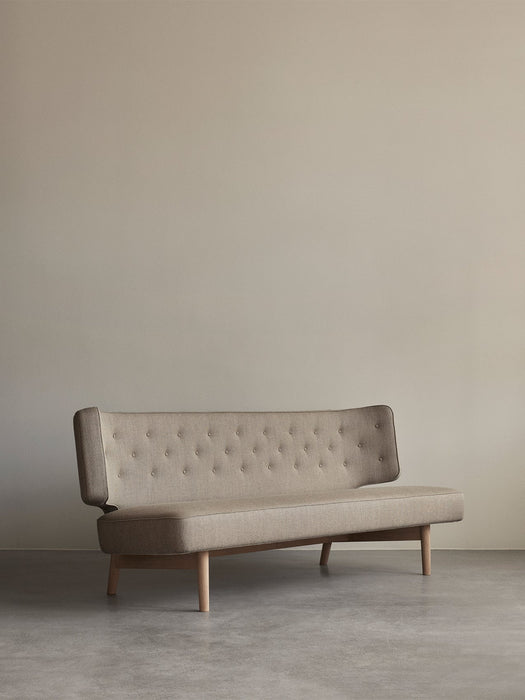 The Radiohus Sofa P2 in light beige upholstery, with a button-tufted backrest and wooden legs, shown in a minimalist room.