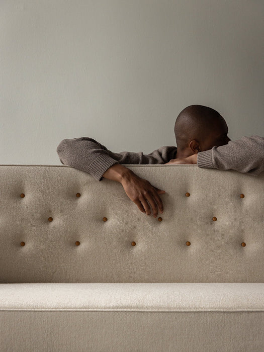 A person rests on the quilted back of the off-white Radiohus Sofa P3, highlighting its tactile texture and button details.