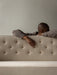 A person rests on the quilted back of the off-white Radiohus Sofa P3, highlighting its tactile texture and button details.