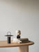 The black Ray Table Lamp, Portable, styled on a light oak table next to a stack of books with a small sculpture on top.