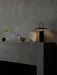 The black Ray Table Lamp provides a warm glow on a dark grey mantelpiece, styled with a ceramic bowl, a vase, and a sprig.