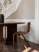 The oak Ready Dining Chair on a stone floor next to a dark table, with a white panelled wall behind.