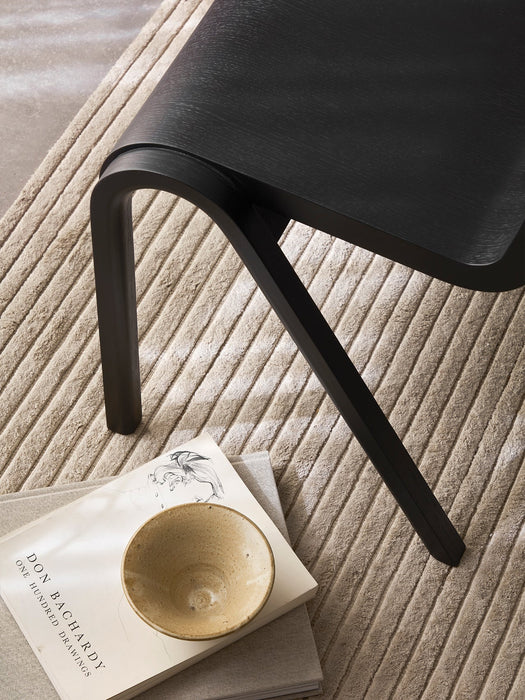Detailed view of the black Ready Dining Chair on a textured beige rug, with a book and a ceramic bowl placed beside its leg.