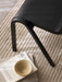 Detailed view of the black Ready Dining Chair on a textured beige rug, with a book and a ceramic bowl placed beside its leg.