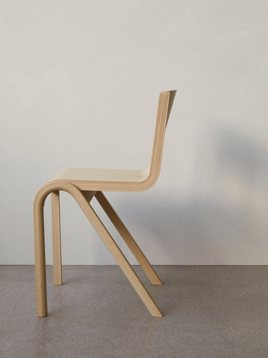 A side-profile of the Ready Dining Chair in natural oak veneer against a white wall, highlighting its cantilevered design.