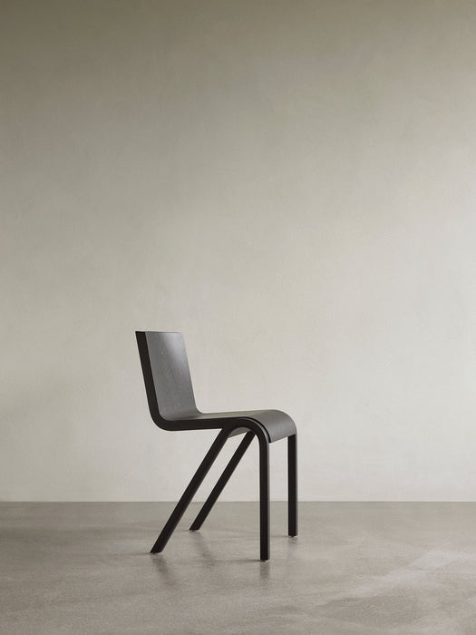 Side view of the black Ready Dining Chair, showcasing its cantilevered silhouette in a minimalist room with a neutral wall.