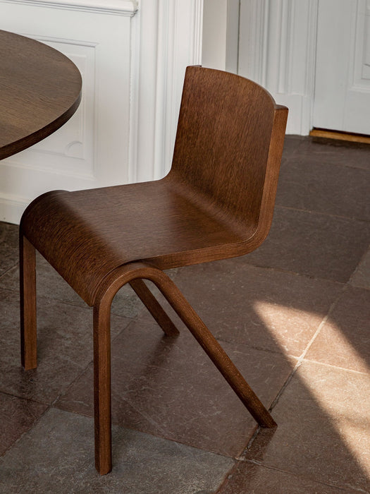 A dark oak Ready Dining Chair with a cantilevered design sits on a stone tile floor next to a matching table.