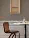 A dark wood Ready Dining Chair is placed next to a sunlit marble table. In the background is a grey wall with framed art.