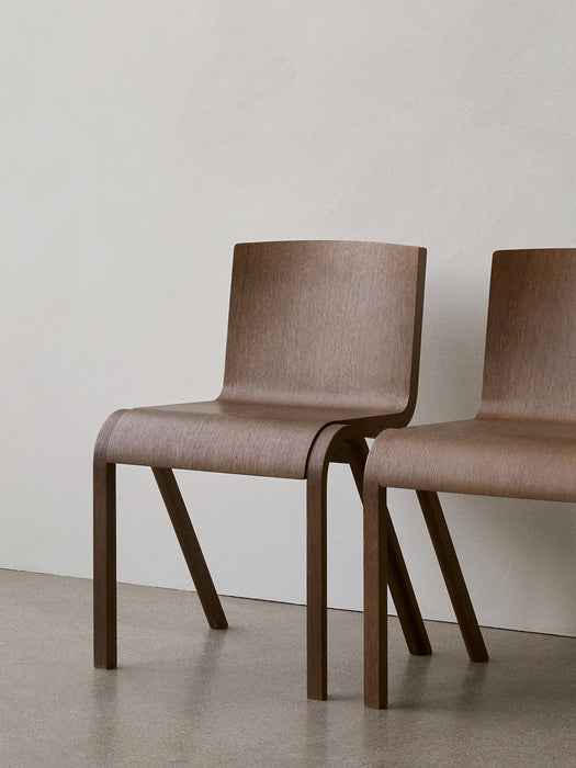 Two Ready Dining Chairs in dark oak veneer, standing side by side in a minimalist space against a light-coloured wall.