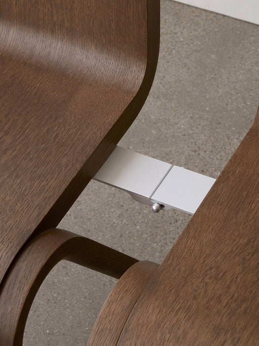 A close-up, overhead view of the silver row-connecting feature linking two dark oak Ready Dining Chairs against a grey floor.