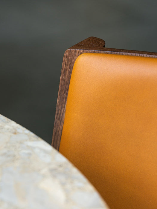 A close-up of the Ready Dining Chair with tan upholstery and dark wood frame beside a marble Harbour Column Dining Table.