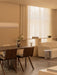 A warmly lit dining room featuring the Androgyne Dining Table, Ready Dining Chairs, Offset Sofa, and Hashira Linear Pendant.