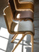 A row of Ready Dining Chairs with upholstered seats in different wood and fabric finishes, lit by sunlight on a grey floor.