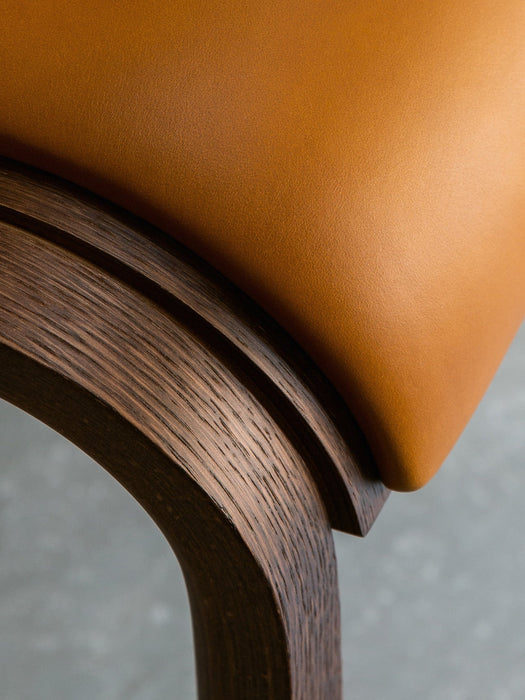 A detail shot of the Ready Dining Chair highlighting the smooth, tan upholstered seat against the textured, dark oak frame.