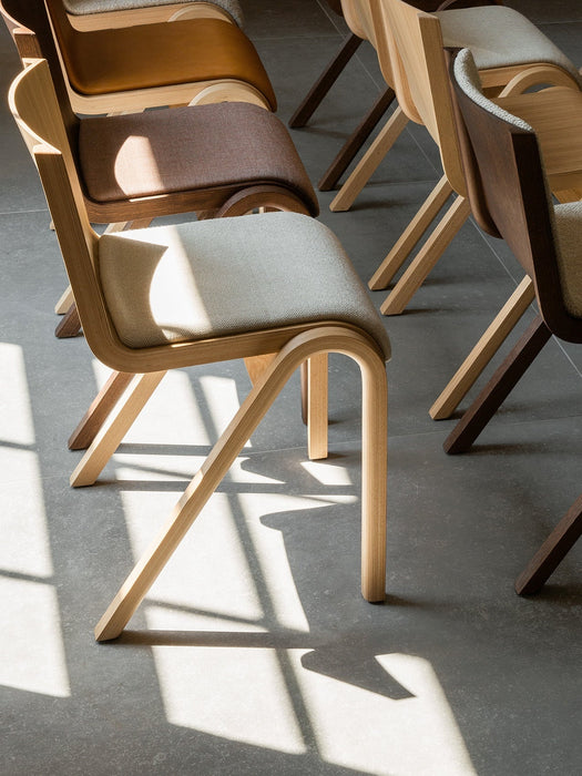 Ready Dining Chairs with upholstered seats in different wood and fabric finishes, arranged in rows on a grey tiled floor.