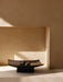 The dark wood Relevé Platter with four figs, placed on a stone surface in a sunlit niche with strong shadows.