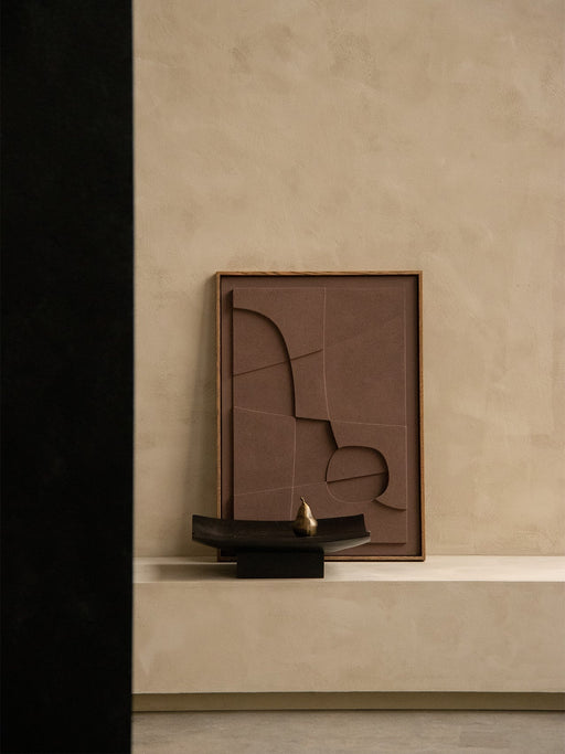 The Audo Releve Platter holding the Sentiment Paper Weight, set on a beige plinth beside a framed, textured artwork.