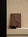 The Audo Releve Platter holding the Sentiment Paper Weight, set on a beige plinth beside a framed, textured artwork.