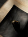The pear-shaped brass Sentiment Paper Weight on the black wood Relevé Platter, lit by sunlight on a wooden floor.