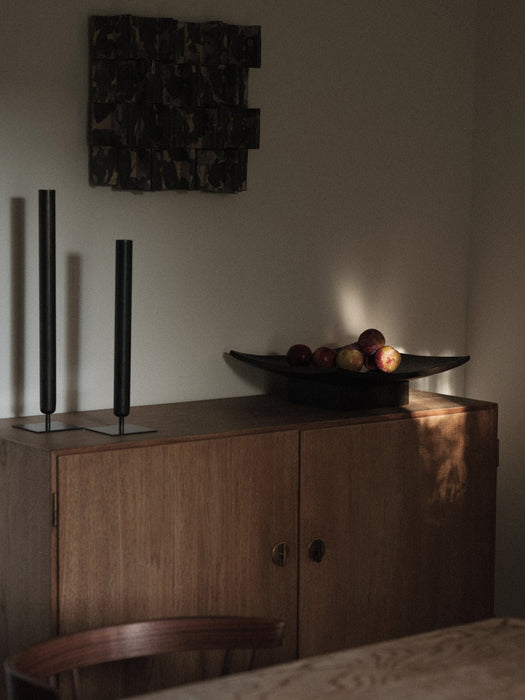 Two tall, black Stance Vases and a Releve Platter with apples, styled on a wooden sideboard in a dimly lit room.