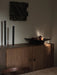 Two tall, black Stance Vases and a Releve Platter with apples, styled on a wooden sideboard in a dimly lit room.