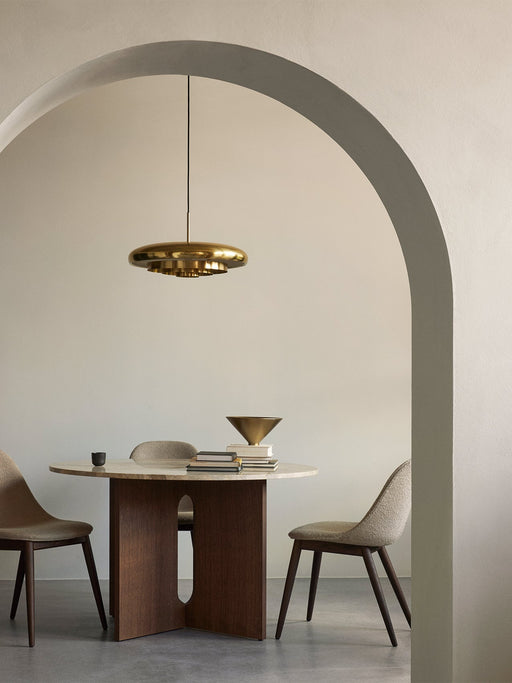A polished brass Resonant Pendant hangs over a marble-topped Androgyne Dining Table in a minimalist dining room setting.