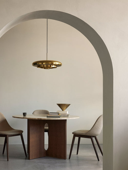 A polished brass Resonant Pendant hangs over a marble-topped Androgyne Dining Table in a minimalist dining room setting.