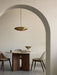 A polished brass Resonant Pendant hangs over a marble-topped Androgyne Dining Table in a minimalist dining room setting.