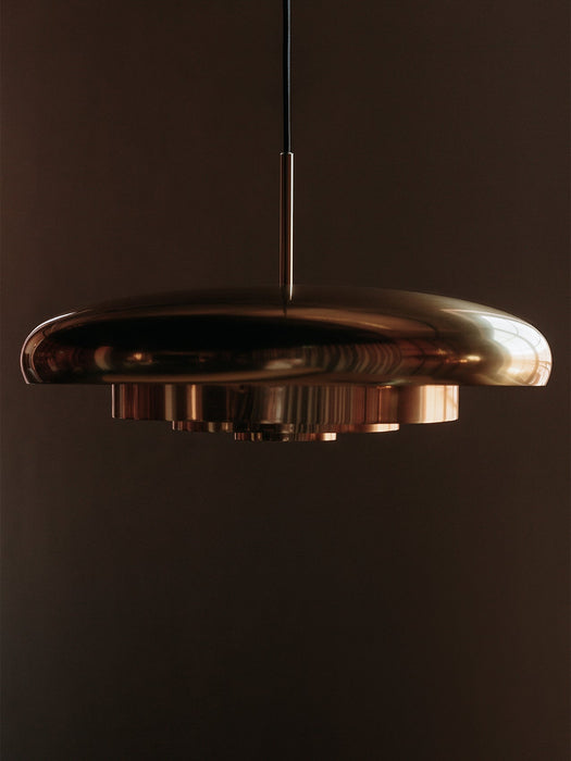 A close-up of the Resonant Pendant in polished brass, its four concentric shades reflecting light against a dark background.