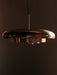A close-up of the Resonant Pendant in polished brass, its four concentric shades reflecting light against a dark background.