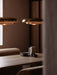 Two polished brass Resonant Pendants illuminate a wooden dining table set with minimalist crockery in a warmly lit room.