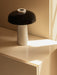 The Reverse Table Lamp with a white Carrara marble base and black shade, sitting on a cream cabinet in warm, direct sunlight.