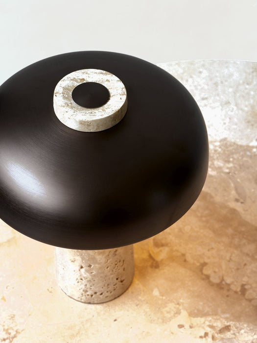 A close-up view of the Reverse Table Lamp, showing its travertine stone base and dimmer switch atop the bronzed shade.