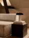 The Reverse Table Lamp on a stack of books atop a black Plinth Cubic table next to a cream Eave Modular Sofa in a cozy room.