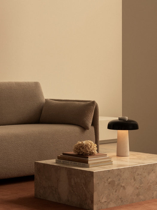 The lit Reverse Table Lamp sits on a stone Plinth Low table beside books and the brown, textured Offset Sofa Bed.