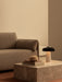 The lit Reverse Table Lamp sits on a stone Plinth Low table beside books and the brown, textured Offset Sofa Bed.