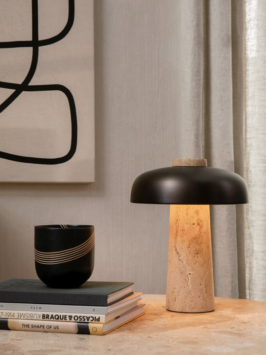 Reverse Table Lamp with travertine base and black shade, lit on a table beside books, a decorative cup, and abstract art.