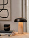 Reverse Table Lamp with travertine base and black shade, lit on a table beside books, a decorative cup, and abstract art.