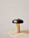 The Reverse Table Lamp, with its lit travertine base and bronzed shade, sits on a marble Harbour Column Lounge Table.