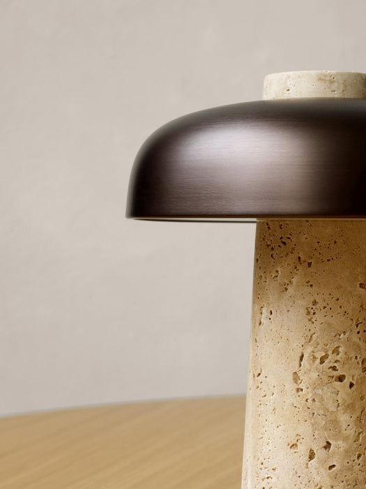 A close-up of the Reverse Table Lamp, highlighting the porous texture of the travertine base and the smooth bronzed shade.