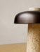 A close-up of the Reverse Table Lamp, highlighting the porous texture of the travertine base and the smooth bronzed shade.