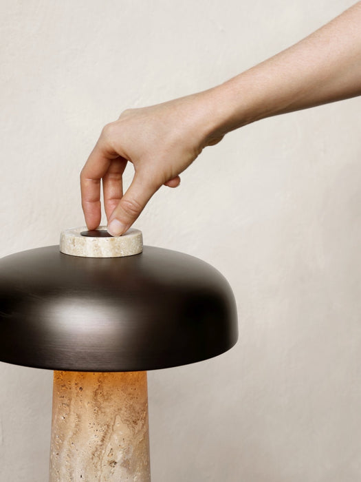 A person's hand adjusts the travertine dimmer switch on the top of the Reverse Table Lamp, which has a bronzed shade.