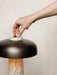 A person's hand adjusts the travertine dimmer switch on the top of the Reverse Table Lamp, which has a bronzed shade.