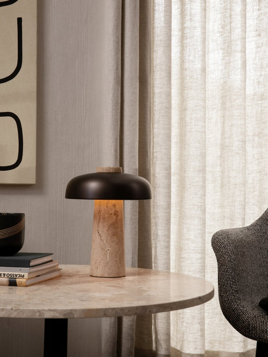 A lit Reverse Table Lamp on a Harbour Column Lounge Table next to a Harbour Lounge Chair in a calm, modern interior.