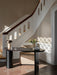 The Reverse Table Lamp sits on a dark oval desk in a sunlit entryway, with a grand white staircase in the background.